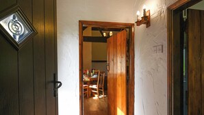A wooden door with a glass panel, a hallway leading to a dining area with a table and chairs, and a wall-mounted light fixture. - 3 bedroom accommodation in Church Stretton (Church Stretton)