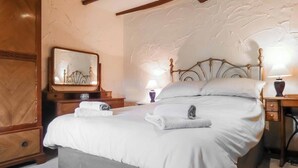 A neatly made bed with white linens and towels, a wooden nightstand with a lamp, a mirror with a cityscape, and a headboard with a decorative design. - 3 bedroom accommodation in Church Stretton (Church Stretton)