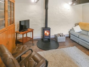 A living room with a fireplace, leather chairs, a television on a stand, and a sofa.
