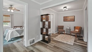 Una sala de estar moderna con piso de madera, una estantería negra en el centro, dos sillones marrones, una pequeña mesa auxiliar con una lámpara y un cuadro en la pared.