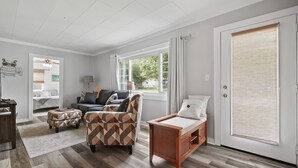 Una sala de estar con sofá, sillón, reposapiés y una pequeña mesa de madera.