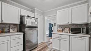 Una cocina moderna con armarios blancos, un refrigerador de acero inoxidable, un microondas y piso de madera.