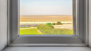 A window with a view of a beach and a fenced area with a green structure. - A beautiful two bedroom apartment with stunning views over Morecambe Bay. (Morecambe)