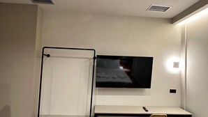 Et moderne værelse med et fladskærms-TV på væggen, trægulv og et simpelt skrivebord med stol.