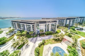 A modern residential complex with multiple high-rise buildings, a central courtyard with palm trees, and a view of the ocean.