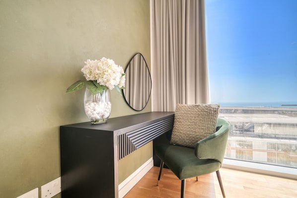 A modern living room with a green armchair, a console table with a vase of flowers, and a view of the city through large windows.