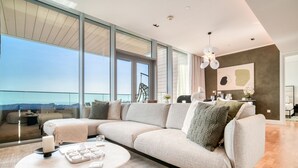 A modern living room with a large sectional sofa, a round coffee table, and a view of the ocean through floor-to-ceiling windows. - Sparkling Balcony Sea View Apt in Bluewaters (Dubai)