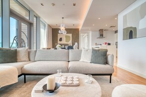 Un salon moderne avec un grand canapé d’angle, une table basse ronde et un coin repas à l’arrière-plan.