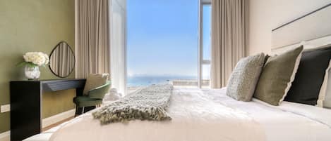 A bedroom with a large bed, a view of the sea, and a window with curtains.