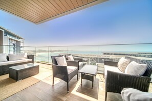 Un balcon doté de meubles en osier, d’une rambarde en verre et offrant une vue sur la mer.