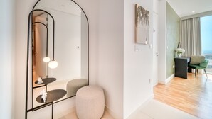 A modern hotel room with a large mirror, a round ottoman, a small table with a sculpture, and a view of the city through large windows. - Sparkling Balcony Sea View Apt in Bluewaters (Dubai)