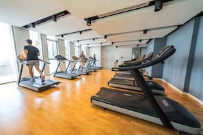 A gym with multiple treadmills, wooden floors, and large windows allowing natural light.