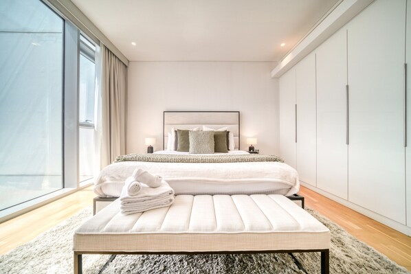 Une chambre moderne avec un grand lit, des lampes de chevet, un banc et une armoire.