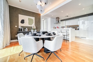 A modern dining area with a round table, white chairs, and a kitchen in the background.