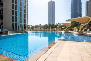 A swimming pool with a tiled deck, surrounded by modern buildings and outdoor seating areas.