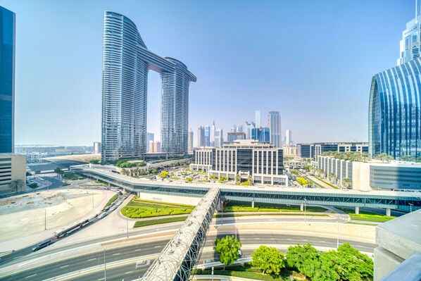 A modern cityscape with high-rise buildings, a central plaza with greenery, and a busy highway.