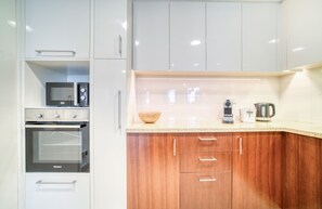 A modern kitchen with white cabinets, a built-in oven, a microwave, and a coffee maker.
