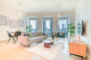 A modern living room with a sofa, coffee table, and chairs, large windows with city views, and artwork on the wall.
