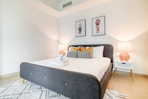 A modern bedroom with a grey upholstered bed, white bedding, and two bedside lamps.