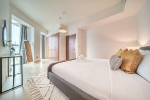 Une chambre moderne avec un grand lit, une table de chevet, un miroir et une vue sur la ville par la fenêtre.