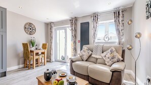 Een moderne woonkamer met een bank, een eethoek met een tafel en stoelen, en een keuken die door een open deur zichtbaar is.