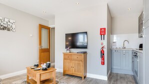 Een moderne keuken met grijze kastjes, een houten tafel en een televisie aan de muur.
