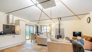 Een moderne keuken met een gasfornuis, een inbouwoven en een roestvrijstalen afzuigkap. Er is een eethoek met een tafel en stoelen, en een woonkamer met een bank en een televisie.
