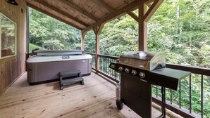 A covered outdoor area with a hot tub, barbecue grill, and a view of a forested area. - Lazy Bear Lodge by Inn & Spa at Cedar Falls (Creola)