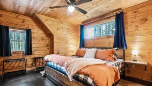 A cozy wooden cabin bedroom with a bed, a ceiling fan, and a window with curtains. - Lazy Bear Lodge by Inn & Spa at Cedar Falls (Creola)