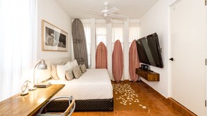 A hotel room with a bed, a desk with a lamp, a television, and a ceiling fan. - 2BR Surf Loft | Beachside with Open Terrace (San José del Cabo)