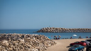 A beach with rocky terrain, a rocky breakwater, and parked cars. - 2BR Surf Loft | Beachside with Open Terrace (San José del Cabo)