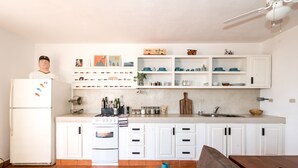A modern kitchen with white cabinetry, a built-in oven, and a dining area with a brown table and a blue cushion. - 2BR Surf Loft | Beachside with Open Terrace (San José del Cabo)