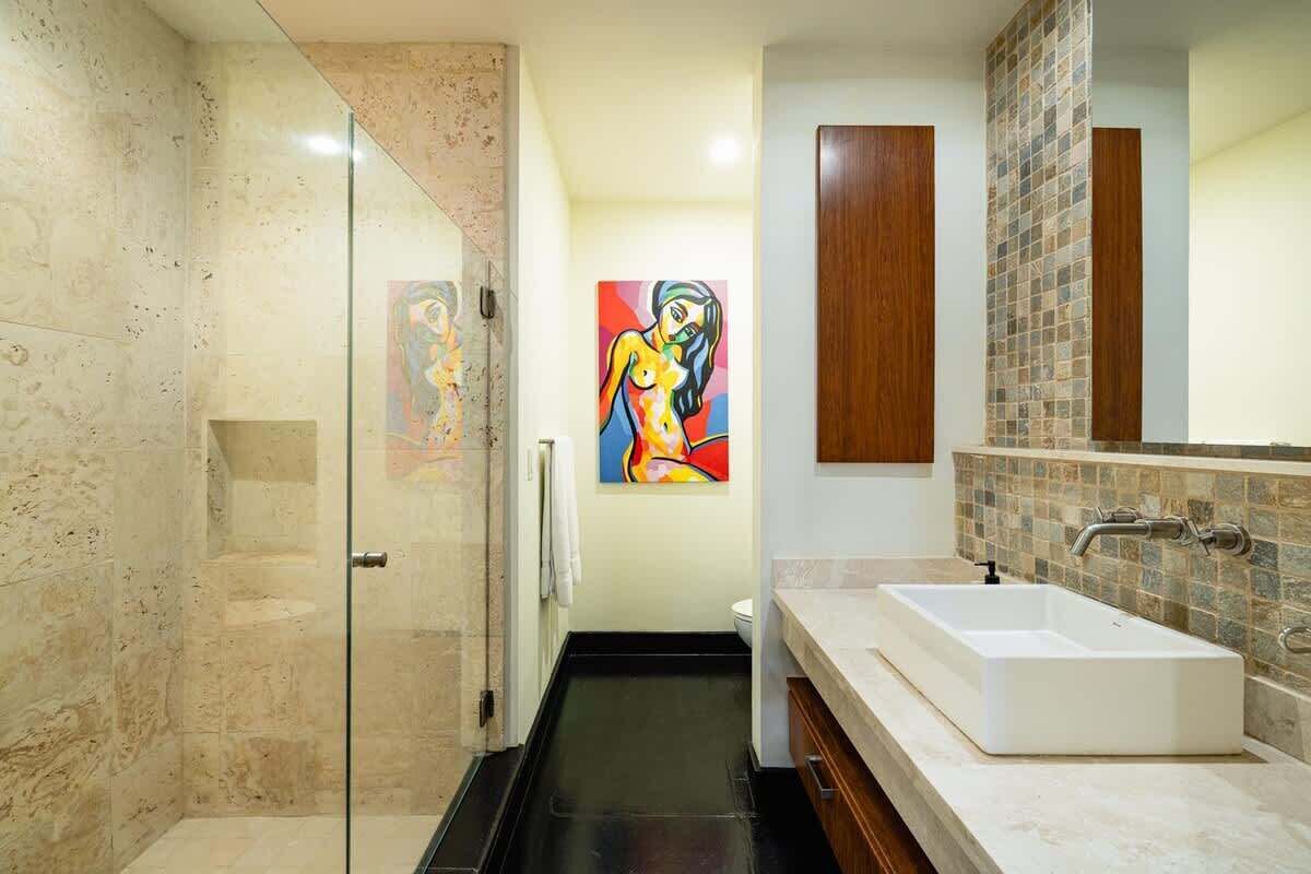 Een moderne badkamer met een douchecabine van glas, een groot rechthoekig wastafelmeubel en een kleurrijk abstract schilderij aan de muur.