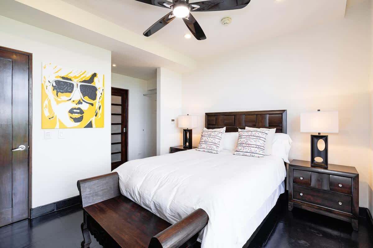 Une chambre d’hôtel avec un grand lit, deux tables de chevet, un ventilateur de plafond et un tableau au mur.
