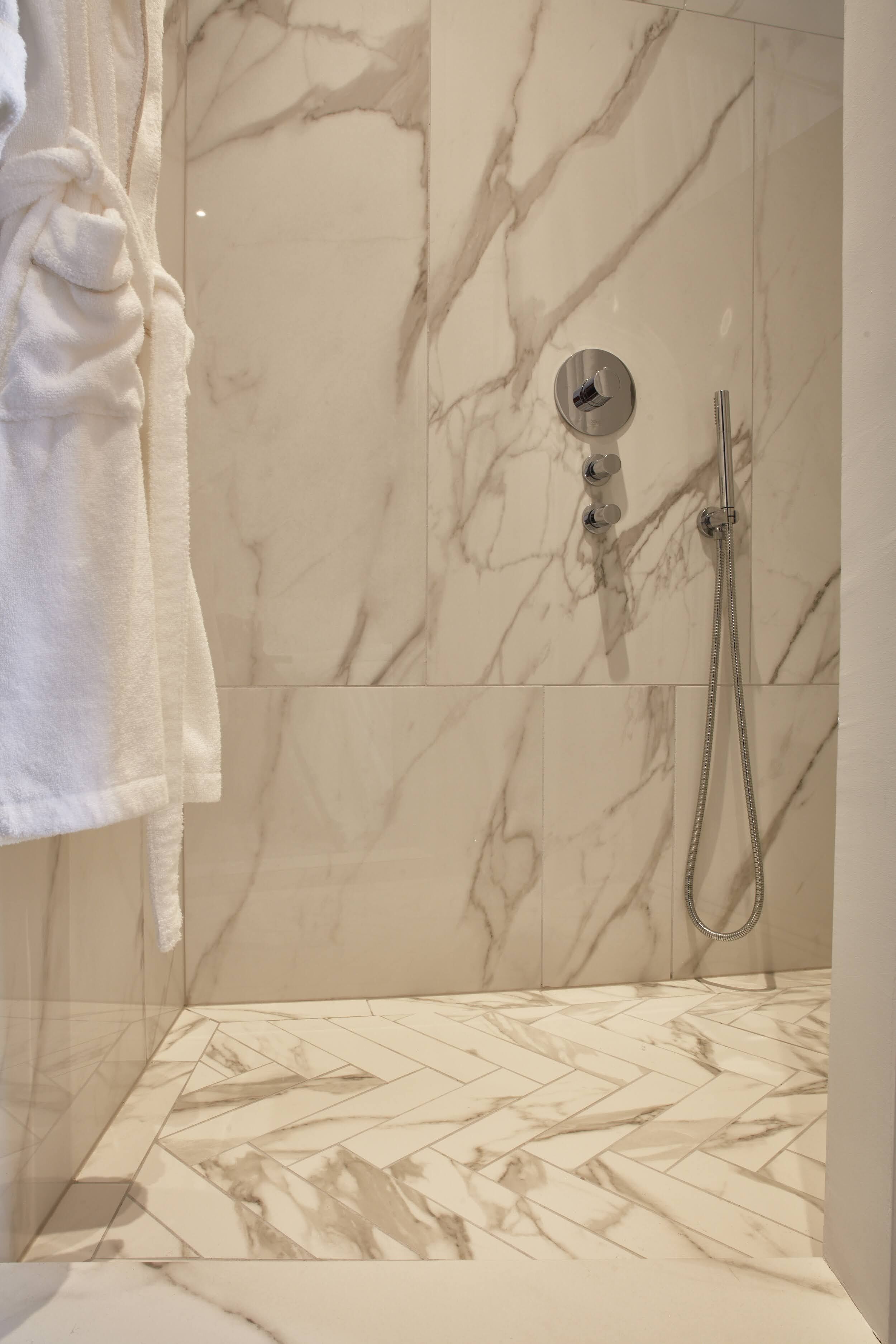A bathroom with marble walls and floor, a shower with a handheld showerhead, and a towel hanging on the wall.