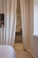 Un dormitorio con cama, espejo y baño visible a través de cortinas.