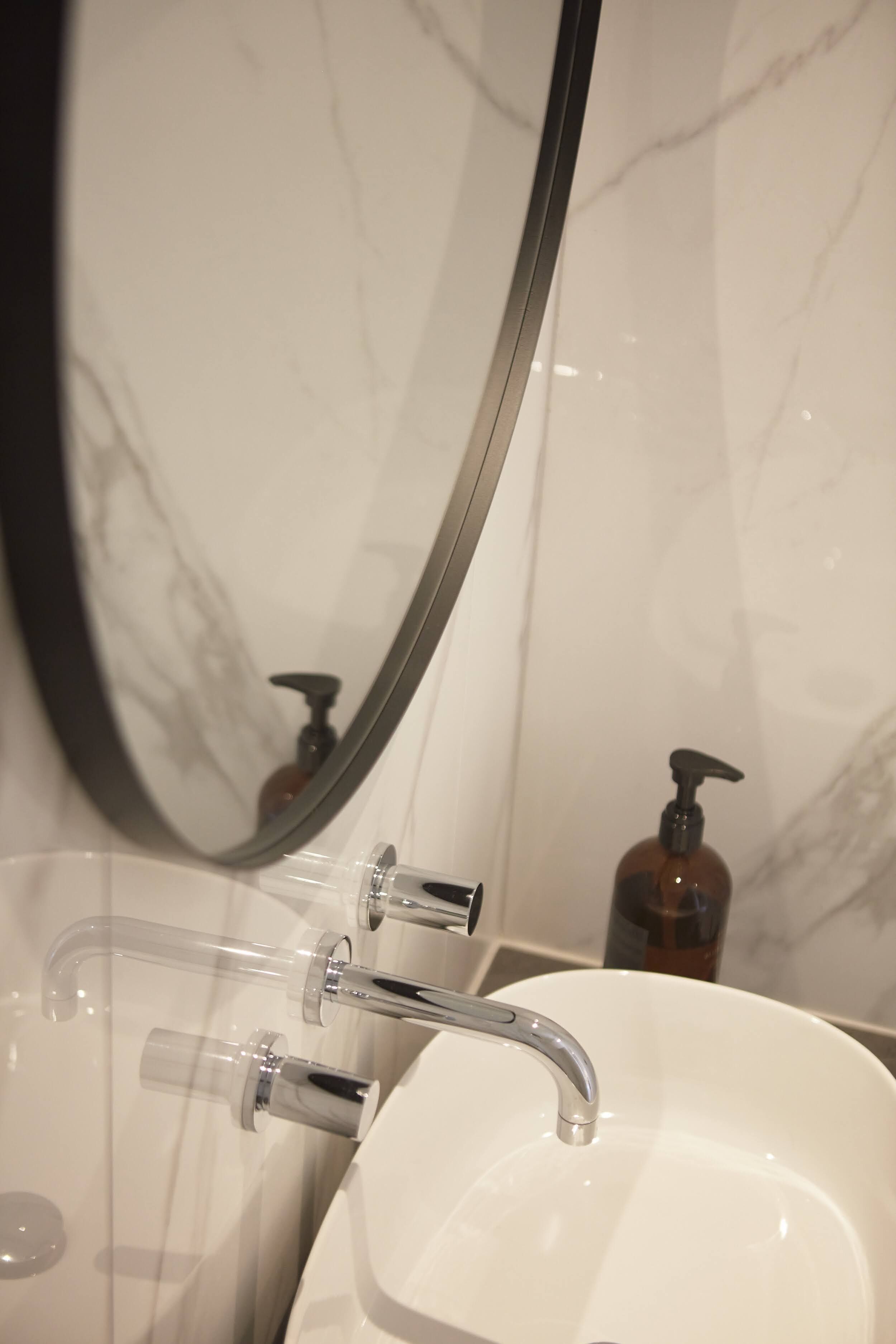 A bathroom with a white sink, a mirror, and a soap dispenser.