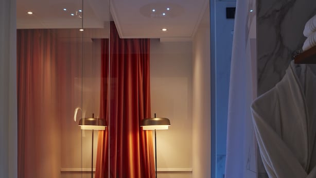A modern bathroom with a glass partition, a chair, a robe, and a floor with a geometric pattern. - The Townhouse (Udine)