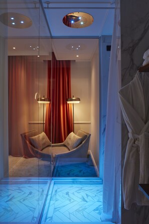 A modern bathroom with a glass partition, a chair, a robe, and a floor with a geometric pattern. - The Townhouse (Udine)