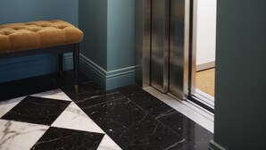 A hallway with a checkered floor, a tufted bench, a geometric mirror, and an elevator. - The Townhouse (Udine)