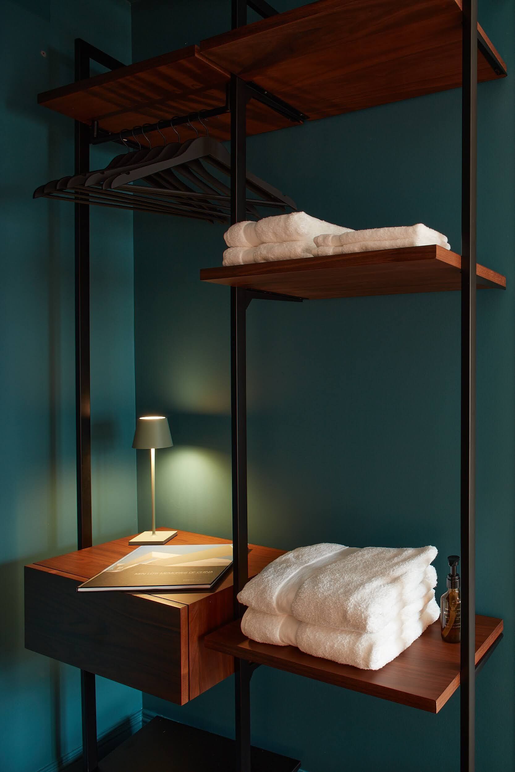 Una cama litera con estructura de madera, una mesita de noche con una lámpara y una toalla doblada en la cama inferior.