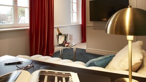 A modern hotel room with a bed, a desk, a TV, and a window with red curtains. - The Townhouse (Udine)