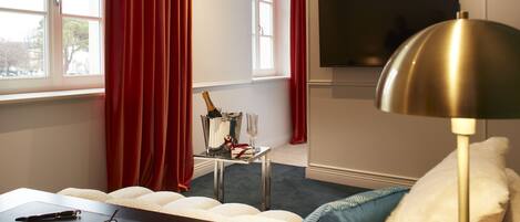 A modern hotel room with a bed, a desk, a TV, and a window with red curtains.