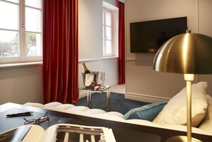 Una habitación de hotel moderna con una cama, un escritorio, un televisor y una ventana con cortinas rojas.