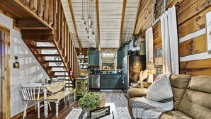 Un interior acogedor con una escalera de madera, un comedor con sillas blancas, una cocina con armarios oscuros y un sofá marrón.