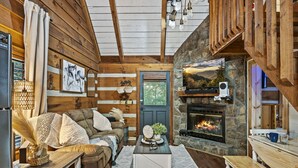 Interior acogedor de una cabaña con chimenea de piedra, paredes de madera, un espacio de estar confortable y una mesa de comedor.