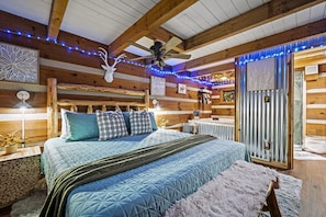 Une chambre située dans un chalet en rondins, avec un grand lit, des poutres apparentes, un ventilateur de plafond et des luminaires décoratifs.