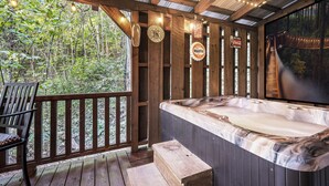 Una terraza de madera con un jacuzzi, una silla de madera y un ventanal grande con vistas a un bosque.