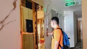 A man in an orange shirt and shorts standing in a hallway with a marble floor, a wooden door, and a green exit sign. - Apartment 2 double bed, modern, new, Nha Trang (Nha Trang)