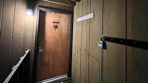 A wooden door with a sign above it, a metal handle, and a small light fixture on the wall. - Tiny cabin in the woods (Sandpoint)